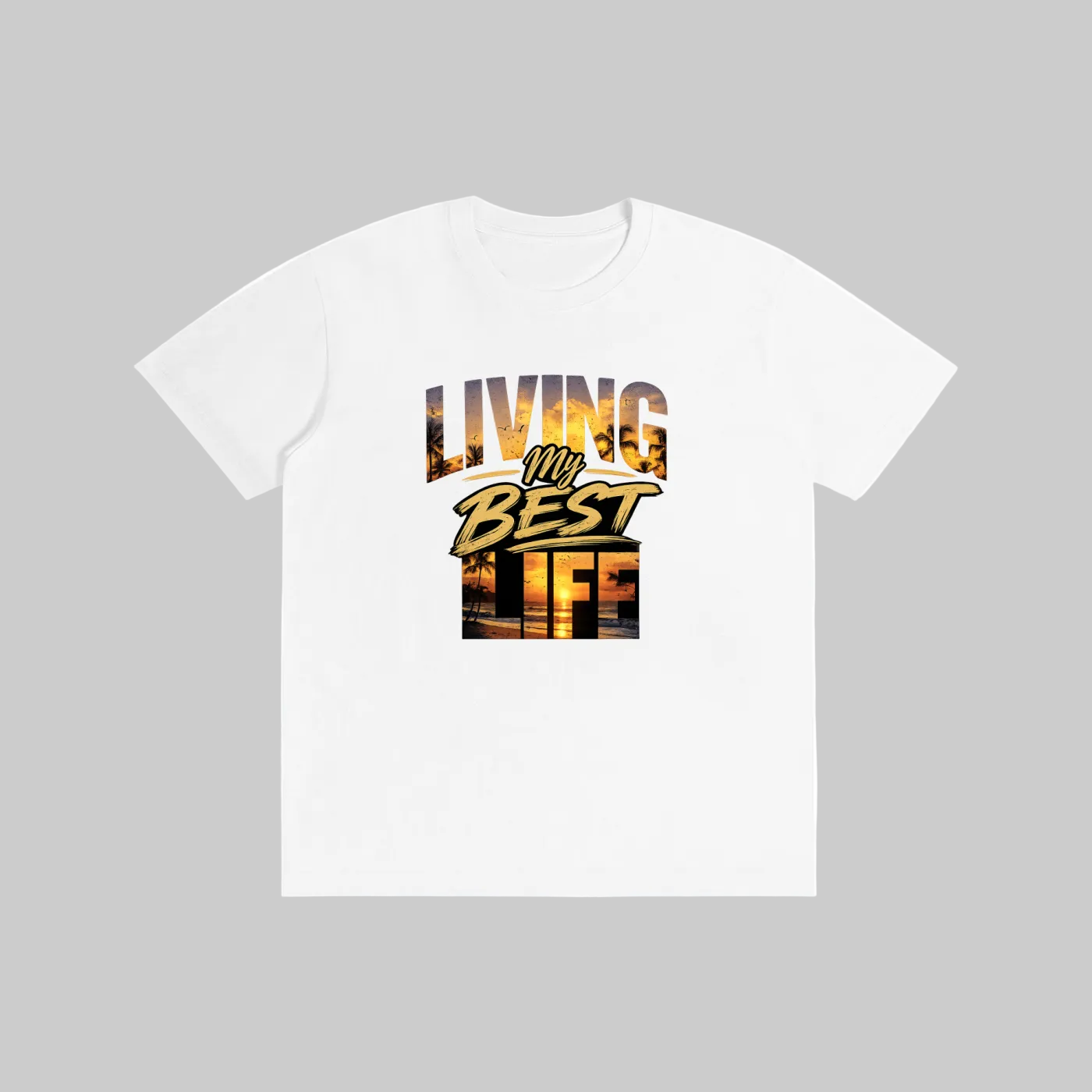 A white short-sleeve crewneck t-shirt featuring a graphic print on the front that reads 'LIVING MY BEST LIFE' in stylized yellow, orange, and black lettering with a sunset landscape design inside the text.